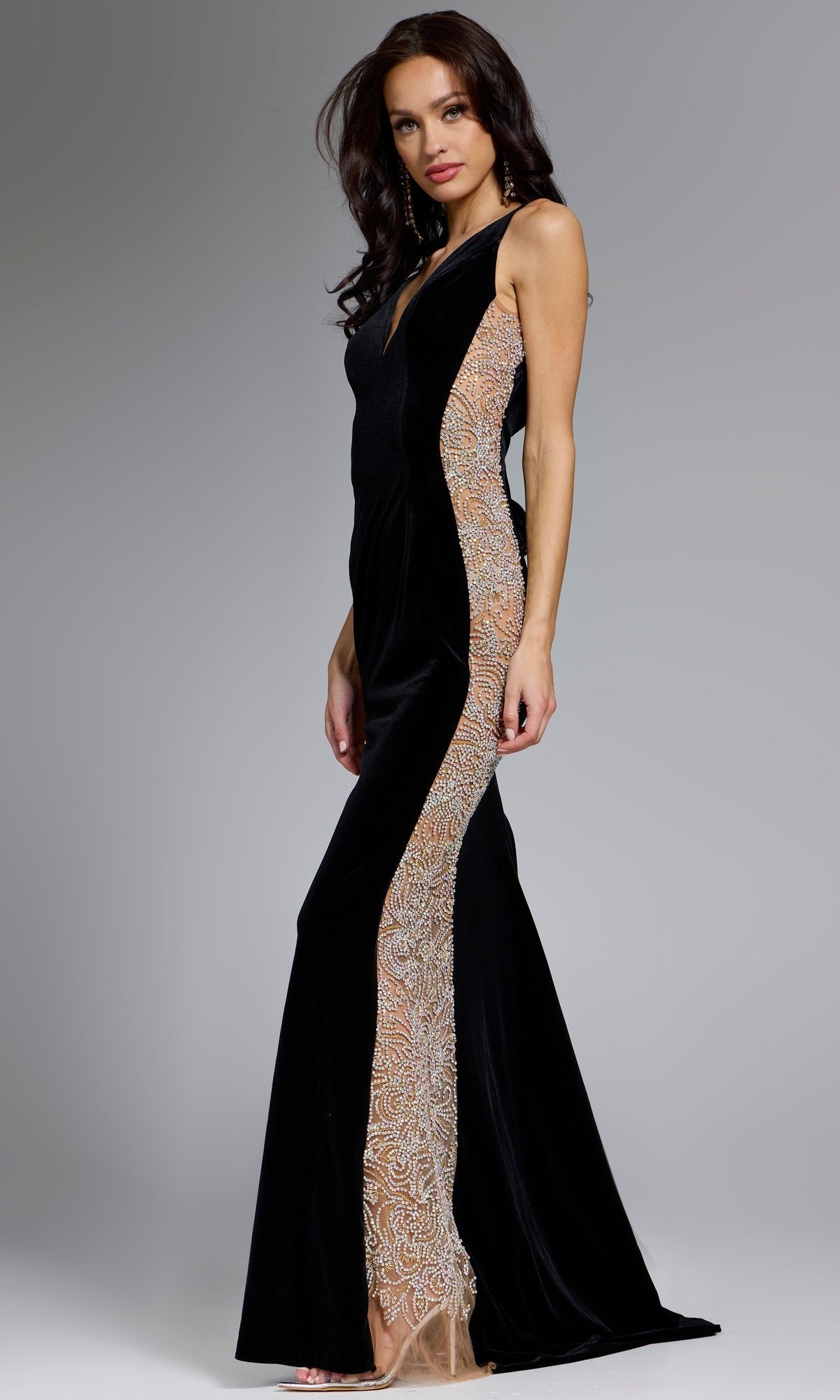 A woman stands in profile against a gray background, wearing the Jovani 42026 Long Prom Dress in black—a fitted sheath evening gown with beaded illusion side panels.